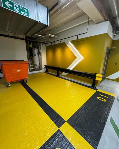Car park level painted yellow and black with fire exit signage and feature chevron wall lighting